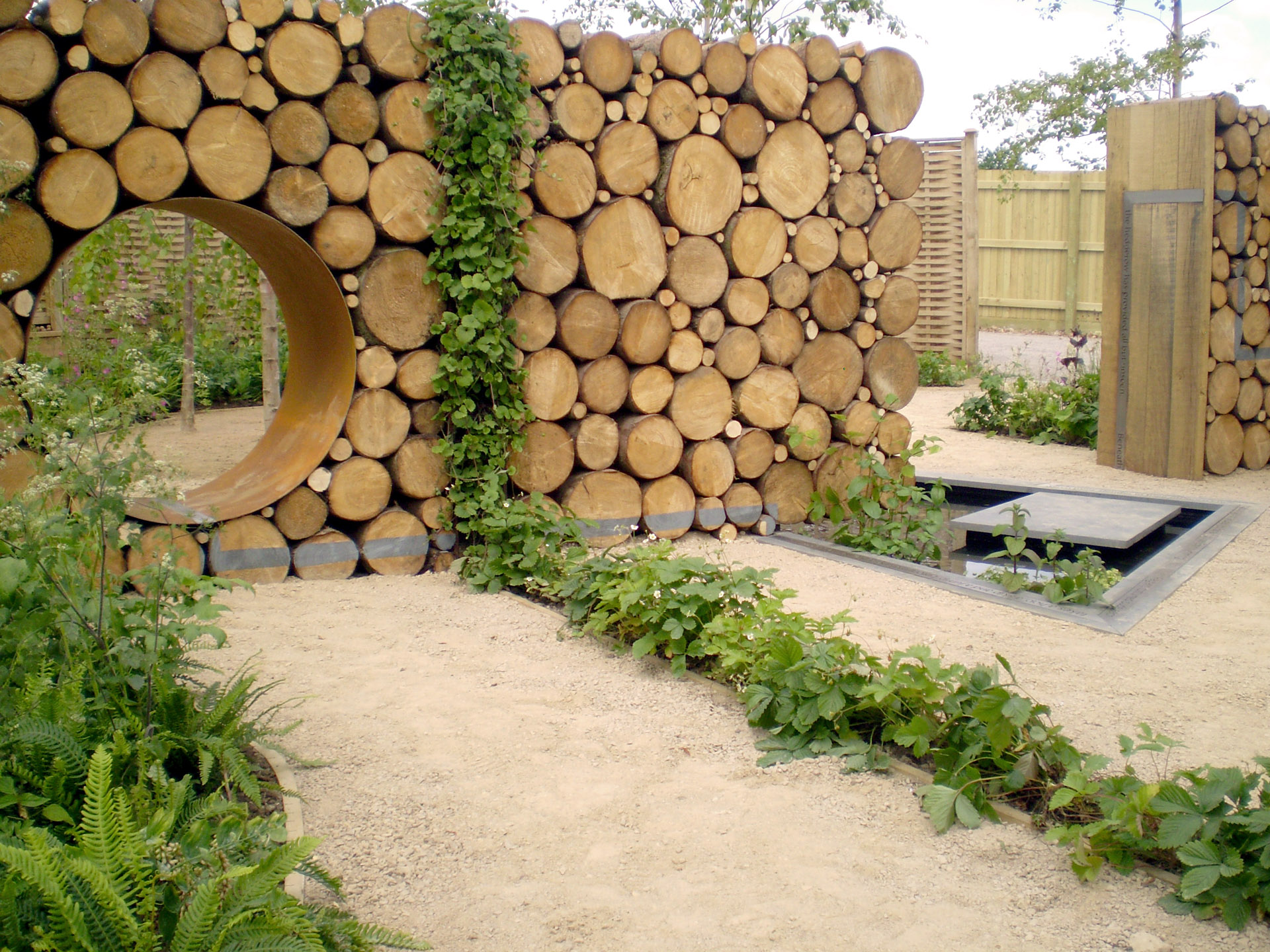 Show garden with wooden partition with hole in it and plants up the side